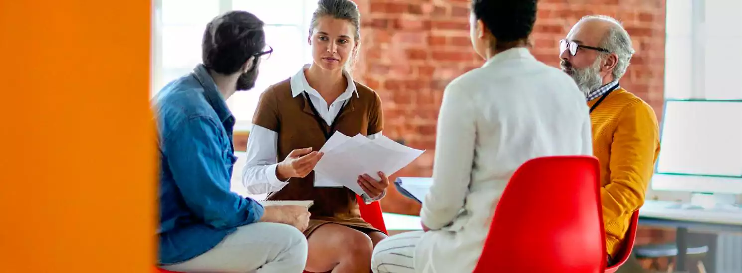 Group discussion among four individuals in a modern office setting, focusing on collaboration and brainstorming for online radio hosting services.